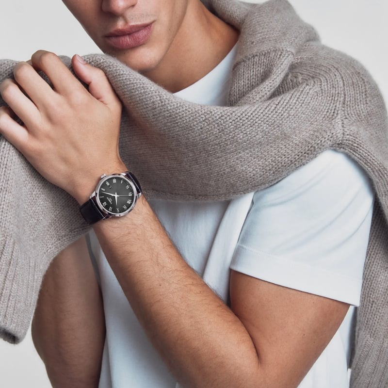 Homme portant une montre Tissot Classic Dream 42mm à cadran noir et bracelet en cuir avec un costume