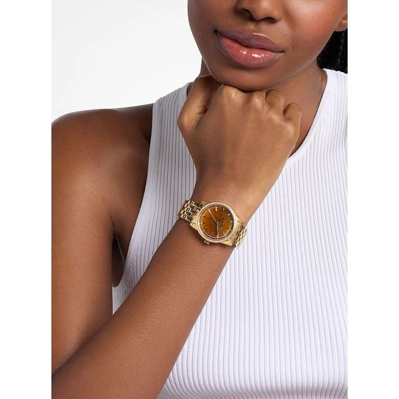 Femme portant la montre Michael Kors Bryant Pavé au poignet, boîtier doré avec tenue élégante décont