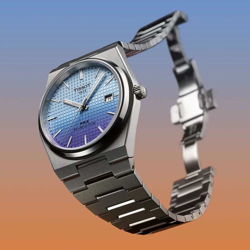 Montre Automatique TISSOT Collection PRX bracelet acier gris mise en scène dans un décor lumineux.