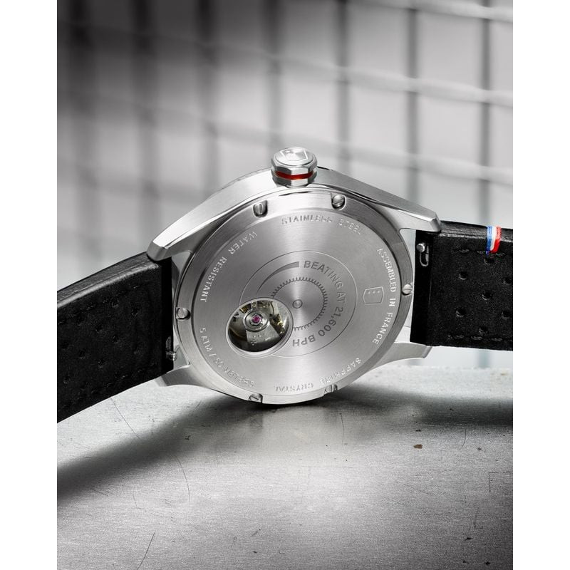 Montre Depancel Autosport posée fond de boîtier vers le haut sur béton, révélant fond acier gravé et