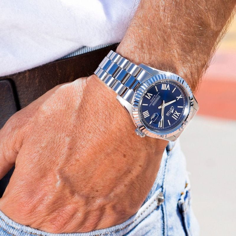 Montre homme Lotus Freedom en acier à cadran bleu portée au poignet, avec chemise blanche, ceinture 