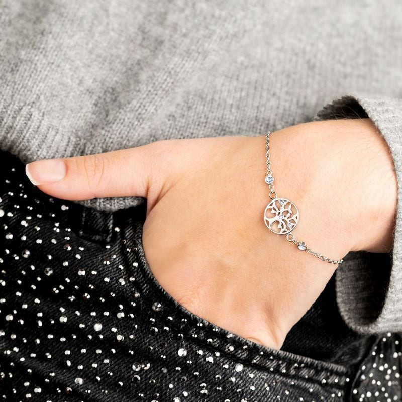Bracelet Lotus Style Arbre de Vie en acier porté au poignet d'une femme, pull en maille gris et pant