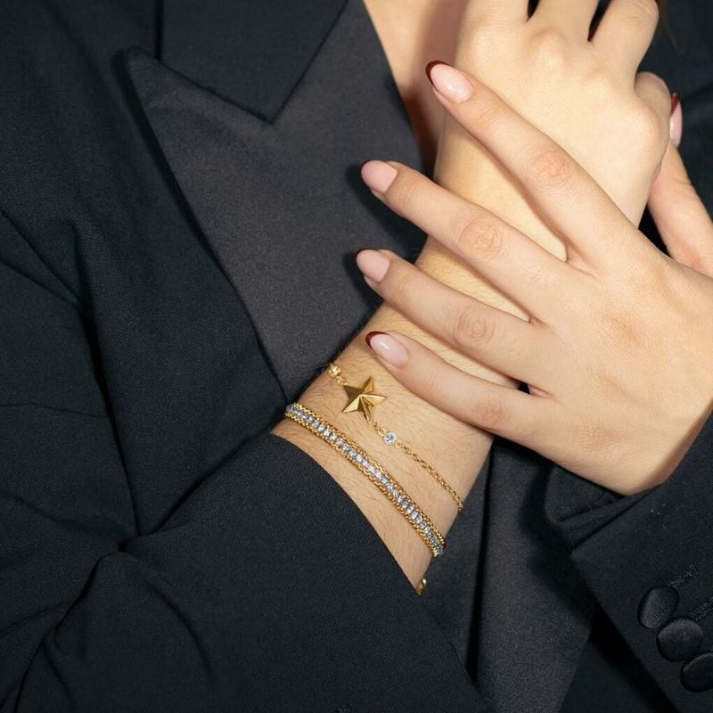 Poignet d'une femme portant des bracelets dorés superposés, dont le bracelet Lotus Style en cristal,