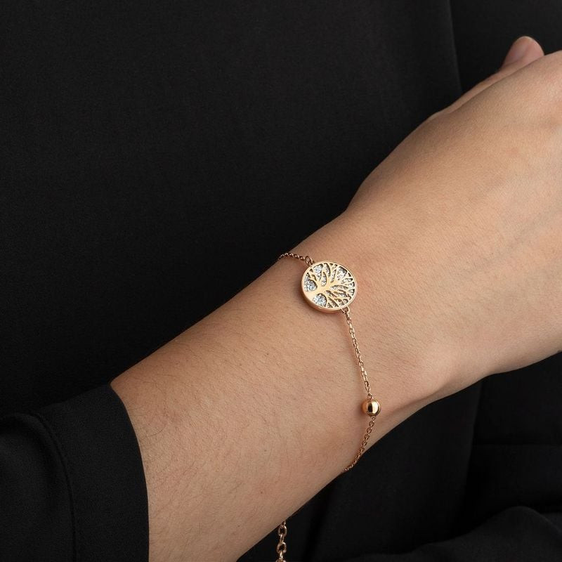 Bracelet Lotus Style Arbre de Vie doré rose porté au poignet d'une femme sur fond de vêtements noirs