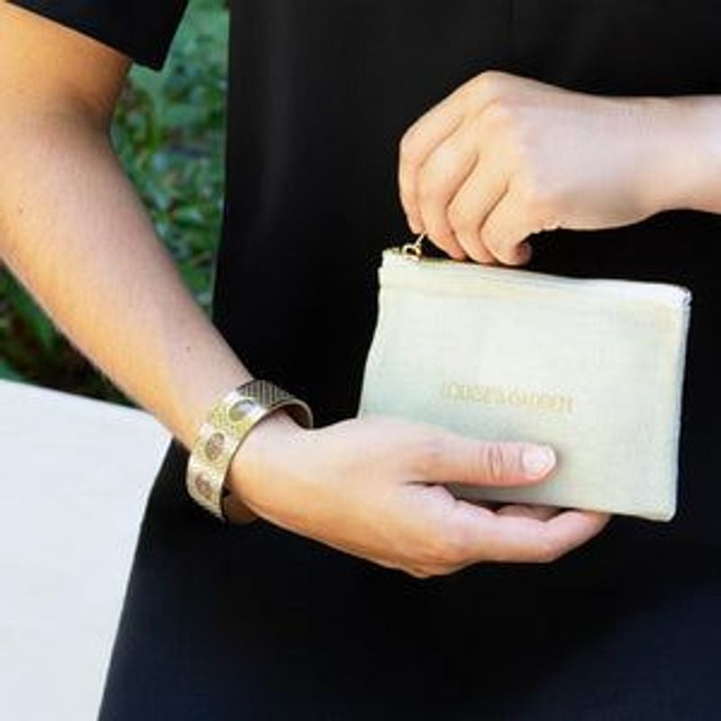 Femme en robe noire portant la manchette dorée Louise's Garden et tenant une pochette zippée vert pâ