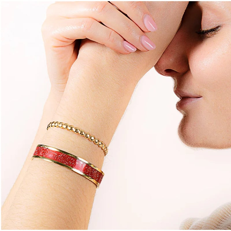 Poignet d'une femme portant le jonc rouge pailleté finition dorée, superposé avec un bracelet perlé 