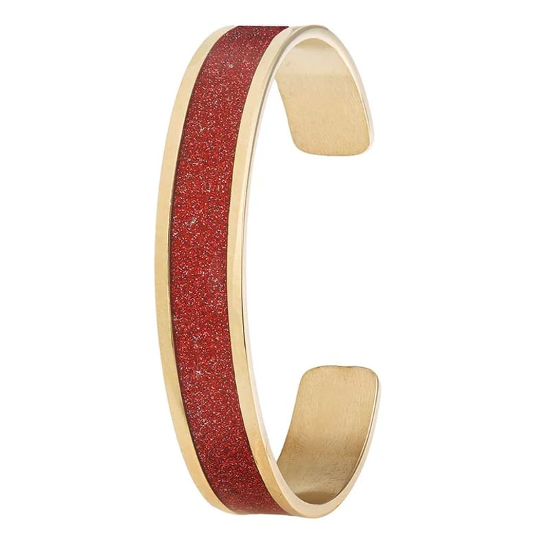 Bracelet jonc ouvert en acier inoxydable doré avec paillettes rouges, présenté de biais sur fond bla