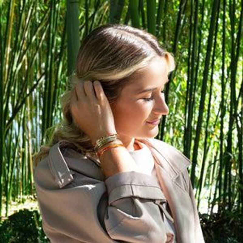 Femme portant la manchette multirangs dorée Louise's Garden à détails orange dans une forêt de bambo