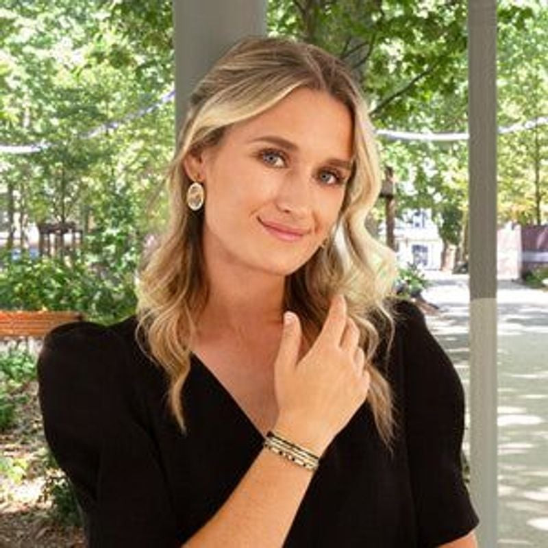 Femme en haut noir souriant à l'extérieur, portant le bracelet manchette Louise's Garden doré et noi