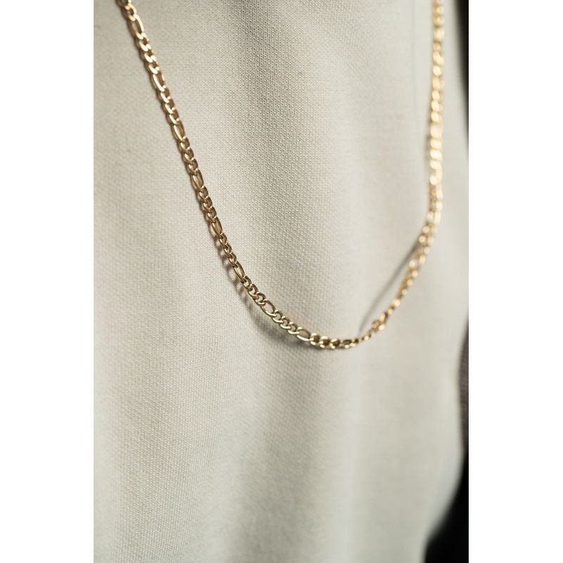 Collier PHEBUS en acier inoxydable doré IP, posé sur un buste en tissu blanc, montrant la texture de