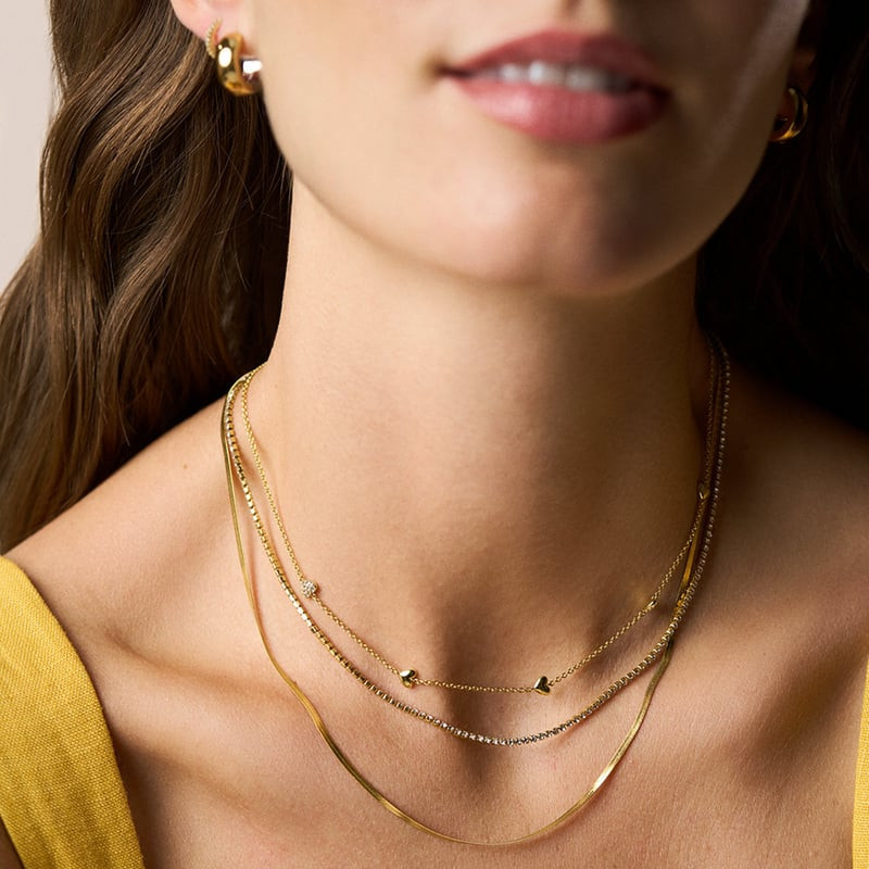 Modèle portant le collier Fossil Sutton Heartbeat superposé à des chaînes dorées et créoles