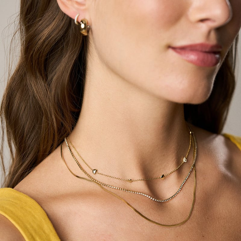 Vue rapprochée de colliers dorés superposés avec la chaîne à cœurs Fossil Sutton Heartbeat