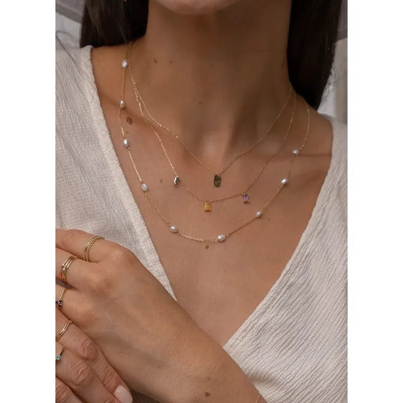Mannequin portant collier Jackie or 14 carats Initiale superposé à des chaînes dorées, perles et bag