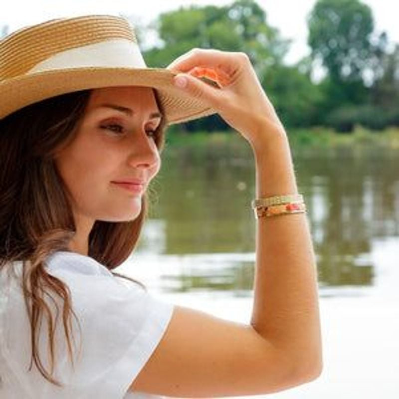 Femme au chapeau de paille portant la manchette Capucine Dorée Louise's Garden au poignet, près d'un