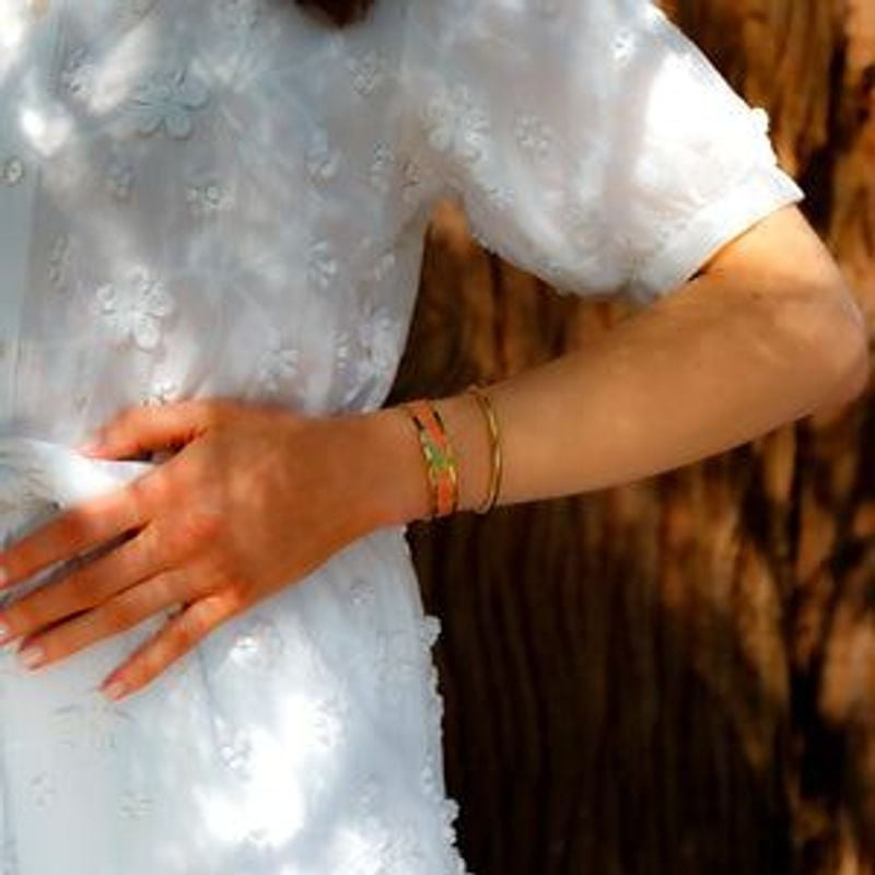 Femme en robe florale blanche portant le jonc Aurore doré Louise's Garden superposé à un bracelet or