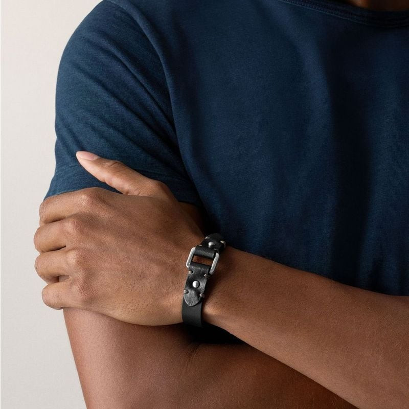 Bracelet Fossil Machine en cuir noir avec surpiqûres dorées, porté au poignet dans un style décontra