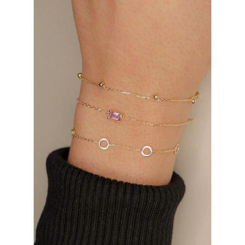 Poignet d'une femme portant des bracelets dorés superposés, dont le bracelet Jackie Gold Bulles à pe