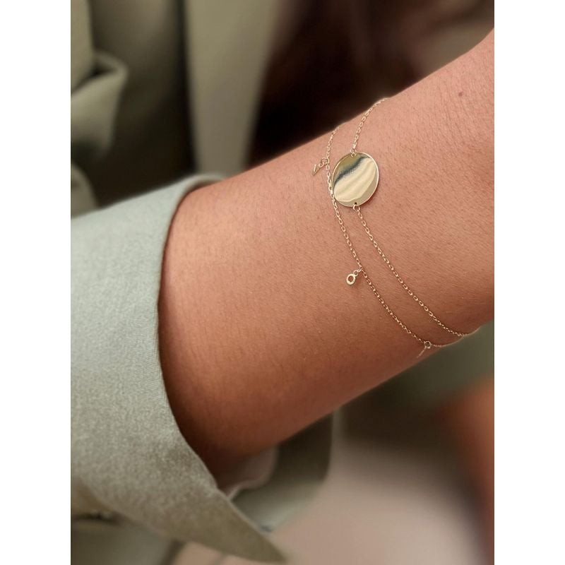 Poignet d'une femme portant le bracelet Jackie Gold L.O.V.E en or jaune 14 carats avec une breloque 