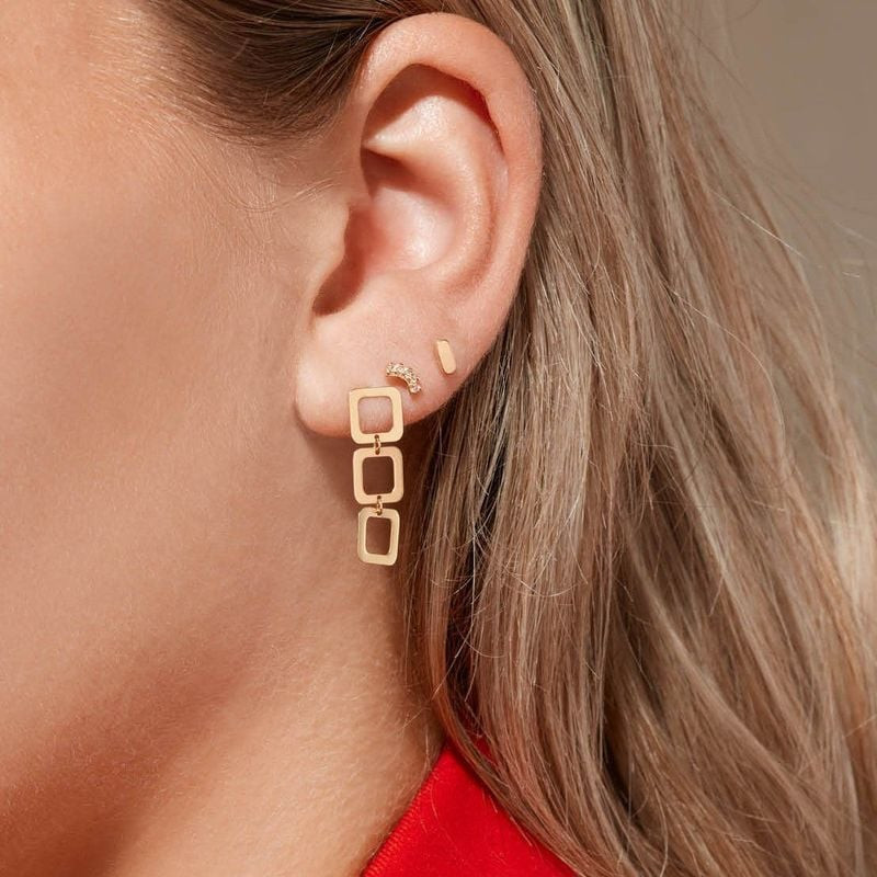 Femme portant des boucles d'oreilles Jackie Gold Laguna 14K à maillons carrés, avec des puces superp