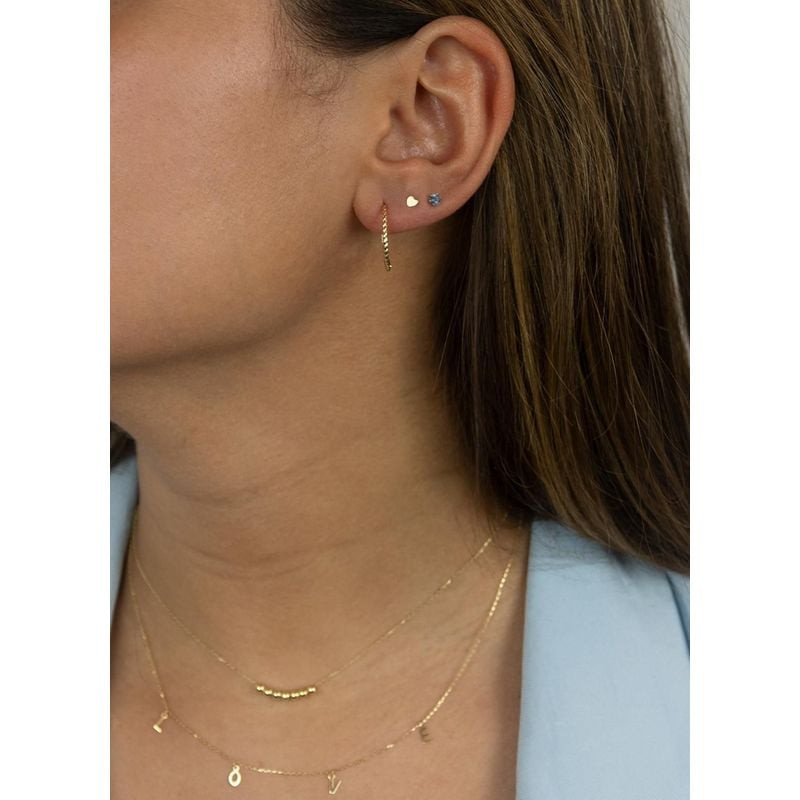 Modèle portant une boucle d'oreille clou mini cœur Jackie Gold 14 carats, avec créole et colliers su