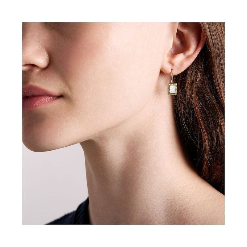 Profil d'un mannequin portant la boucle d'oreille Fossil Raquel dorée, mettant en valeur la pendante