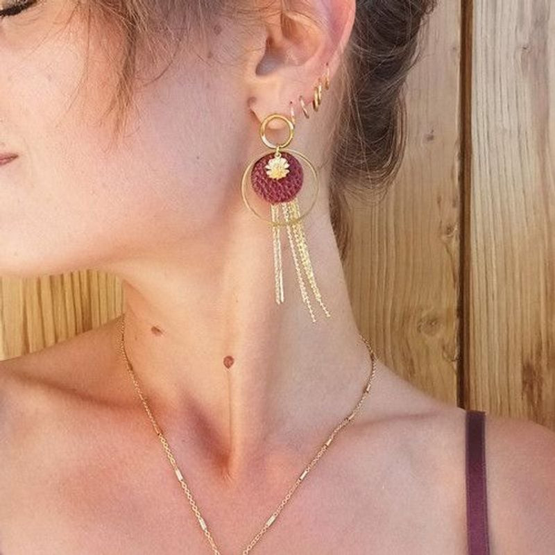 Femme portant une boucle d'oreille pendante Cécile Léonard, fleur en cuir bordeaux et pampilles doré