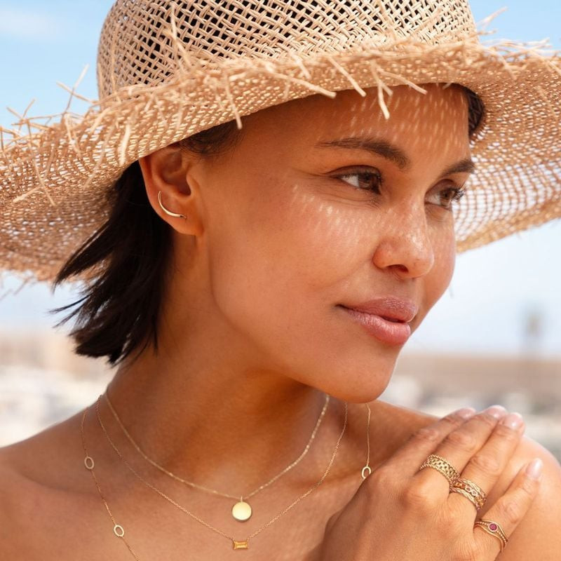 Femme portant une boucle d'oreille Jackie Gold Beaulieu en or 14 carats à l'oreille, chapeau de pail