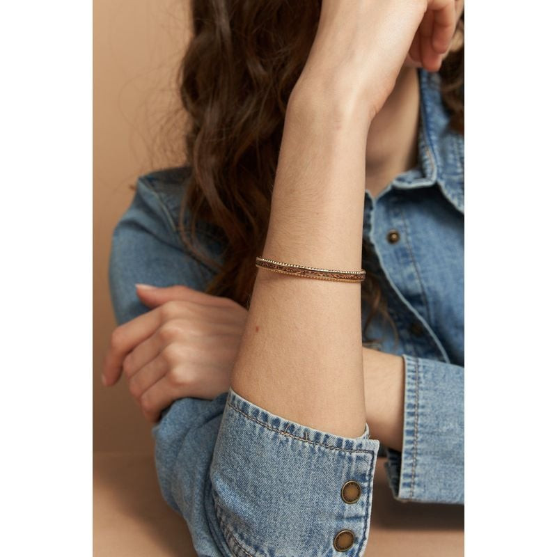 Femme portant le jonc Tuesday doré avec incrustation de cuir camel imprimé léopard au poignet, assoc
