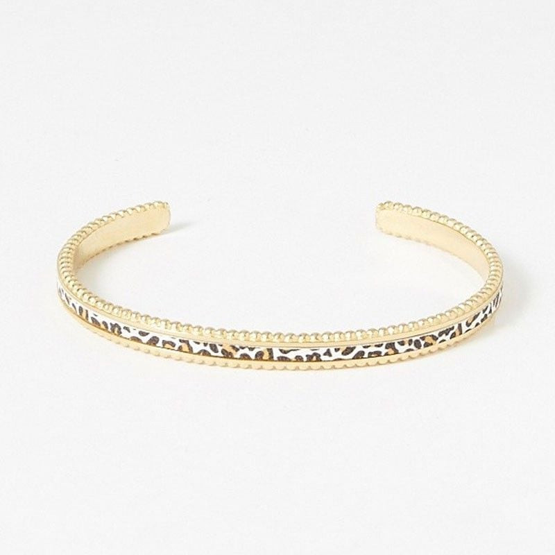 Vue de face du bracelet jonc doré avec bande en cuir blanc imprimé léopard et bords perlés sur fond 