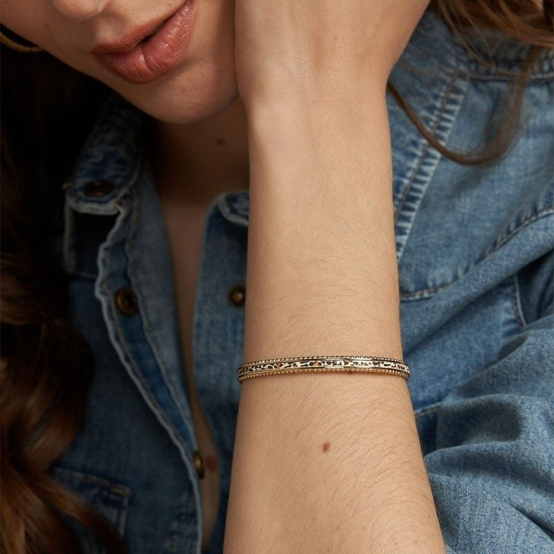 Femme portant le bracelet jonc doré avec cuir blanc imprimé léopard au poignet, stylée avec une vest