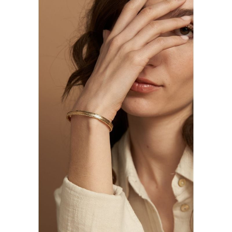 Femme aux cheveux ondulés portant le fin bracelet jonc Tuesday Metallic Gold au poignet, main levée 