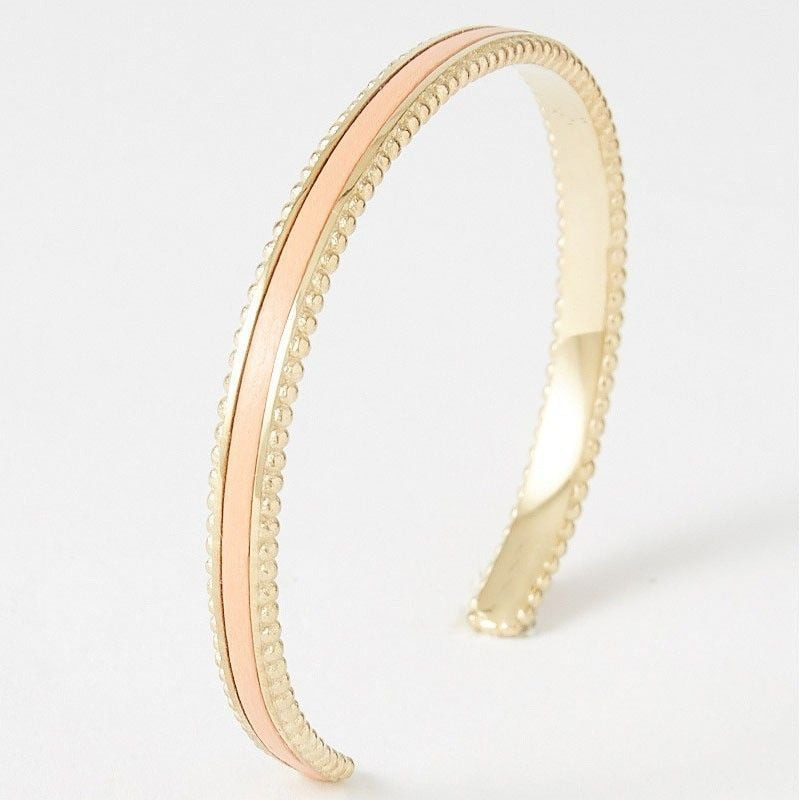 Bracelet jonc ouvert en acier plaqué or, bords perlés et incrustation cuir, présenté de biais sur fo