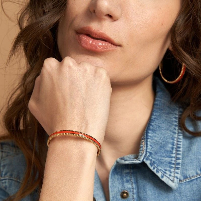 Bracelet jonc FLOWERSFORZOE en acier doré et cuir orange porté au poignet, look élégant et coloré