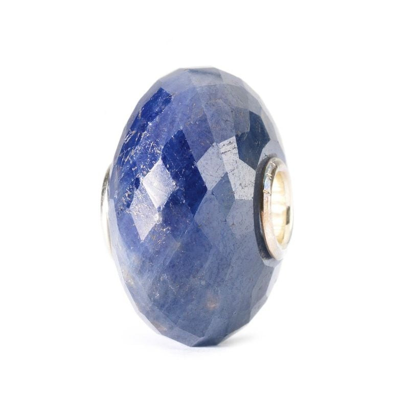 Packshot incliné de la perle Trollbeads Saphir bleue facettée montrant la texture naturelle et le cœ