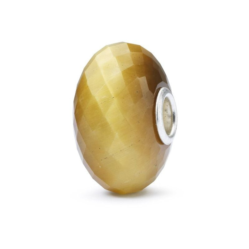 Charme Trollbeads en quartz œil-de-chat facetté, reflets miel doré et cœur en argent poli, sur fond 