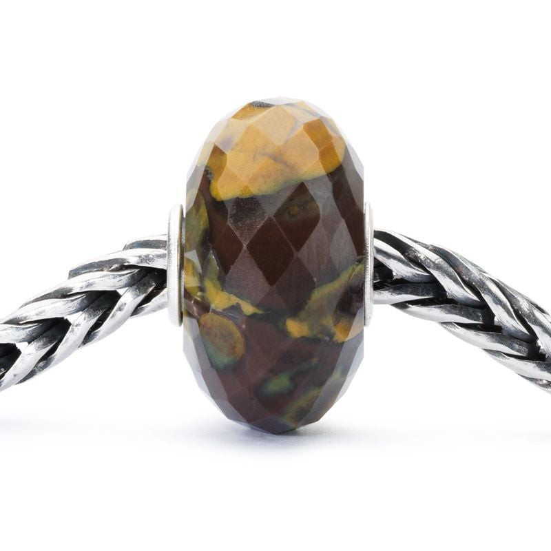 Gros plan sur la bille de calcite Trollbeads facettée et ses inclusions ambre, brunes et olive, brac