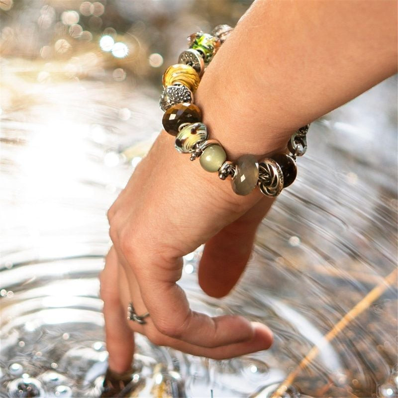 Gros plan d'un bracelet Trollbeads avec perles en verre et argent au poignet au-dessus d'une eau sci