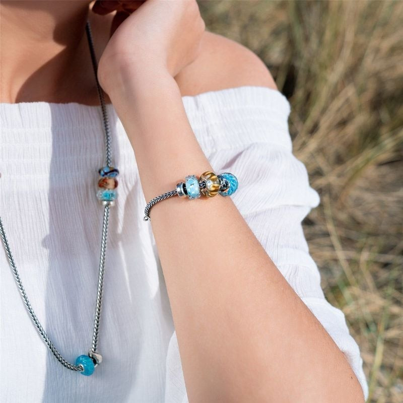 Femme portant un bracelet et un collier Trollbeads avec la perle Vue sur Mer, haut blanc à volants, 