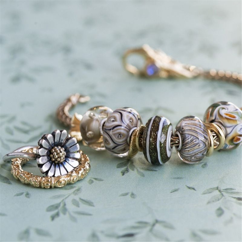 Bille en verre Willow de Trollbeads présentée sur un bracelet doré avec bague marguerite et autres c