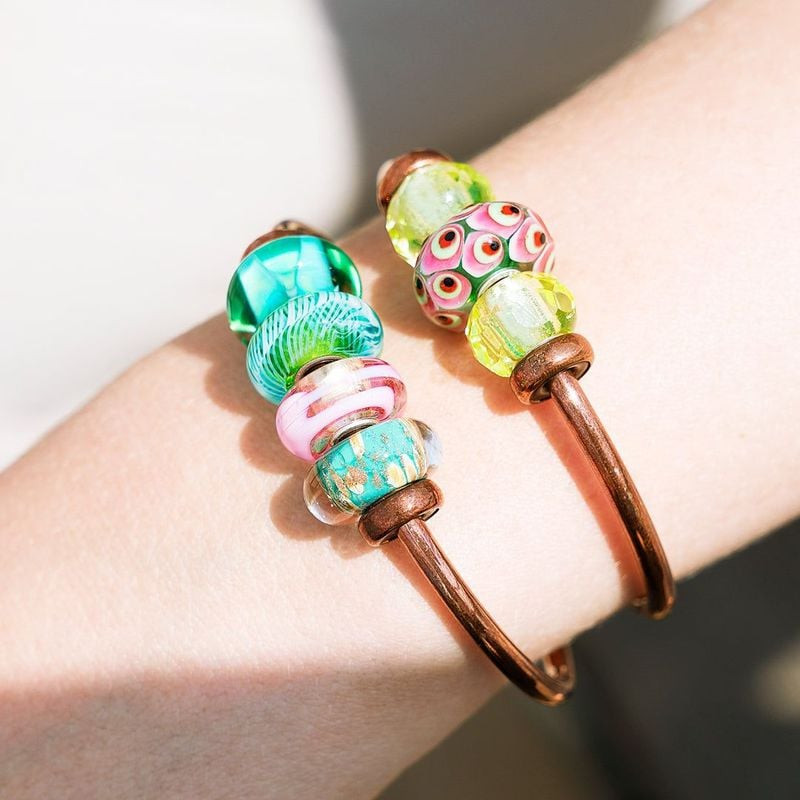 Perle Trollbeads Plume turquoise empilée sur des joncs en cuivre portés au poignet avec d'autres bre