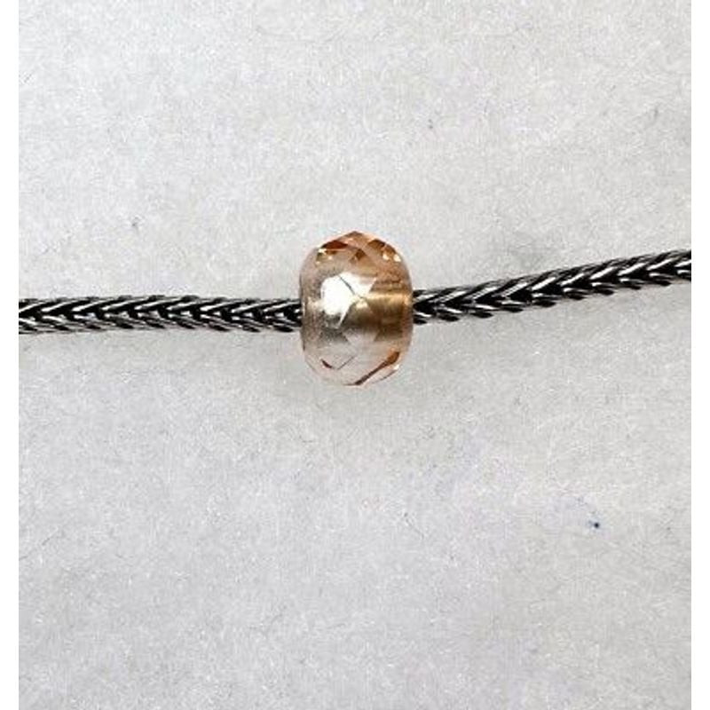 Perle de charme Trollbeads Prisme rose en verre sur cordon tressé, fond papier texturé blanc