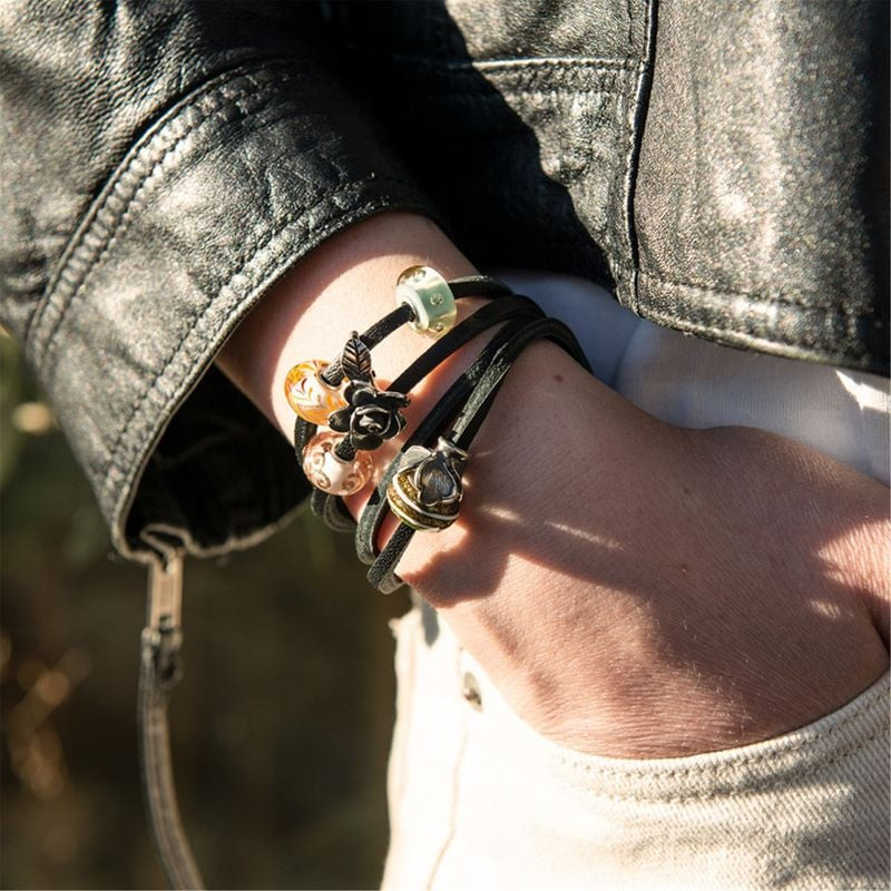 Poignet féminin avec bracelet Trollbeads en cuir noir, charm Rose de la Beauté en argent et perles e
