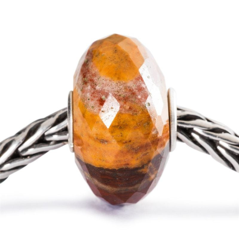 Perle Trollbeads calcédoine brune et jaune enfilée sur un bracelet chaîne en argent en gros plan d'a