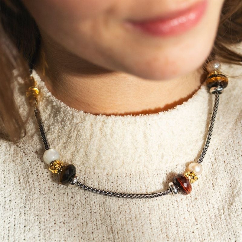 Perle Trollbeads œil de tigre rouge sur collier tressé avec perles et accents dorés portée par un ma