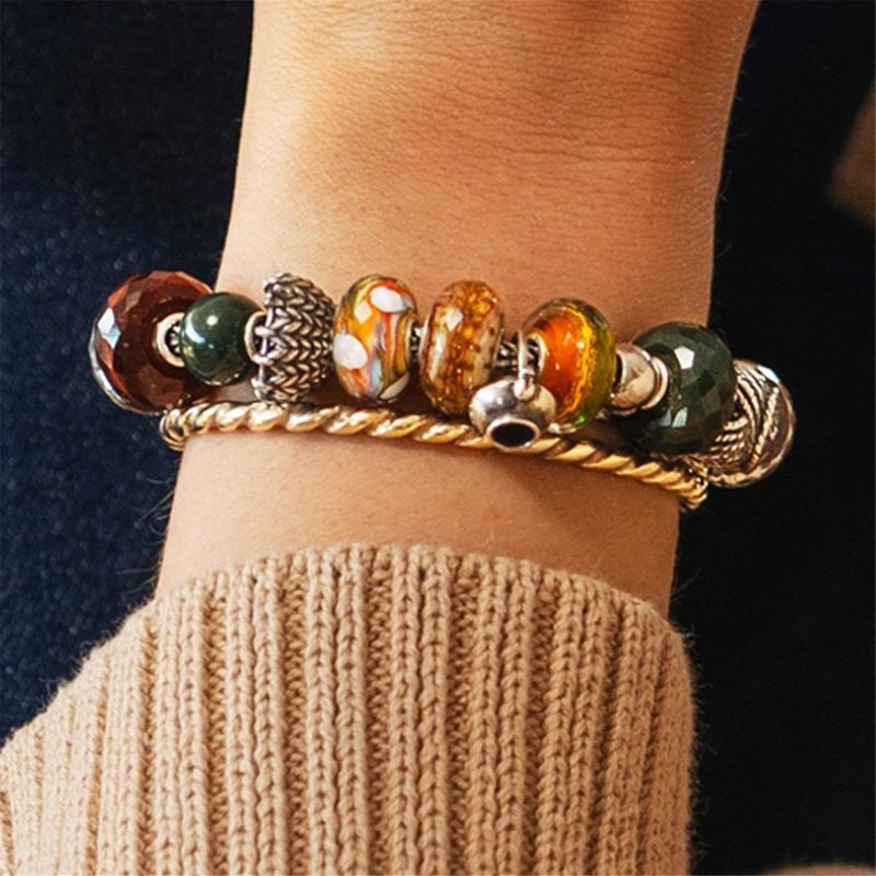 Poignet portant un bracelet Trollbeads en or avec une perle œil de tigre rouge, des perles en verre 