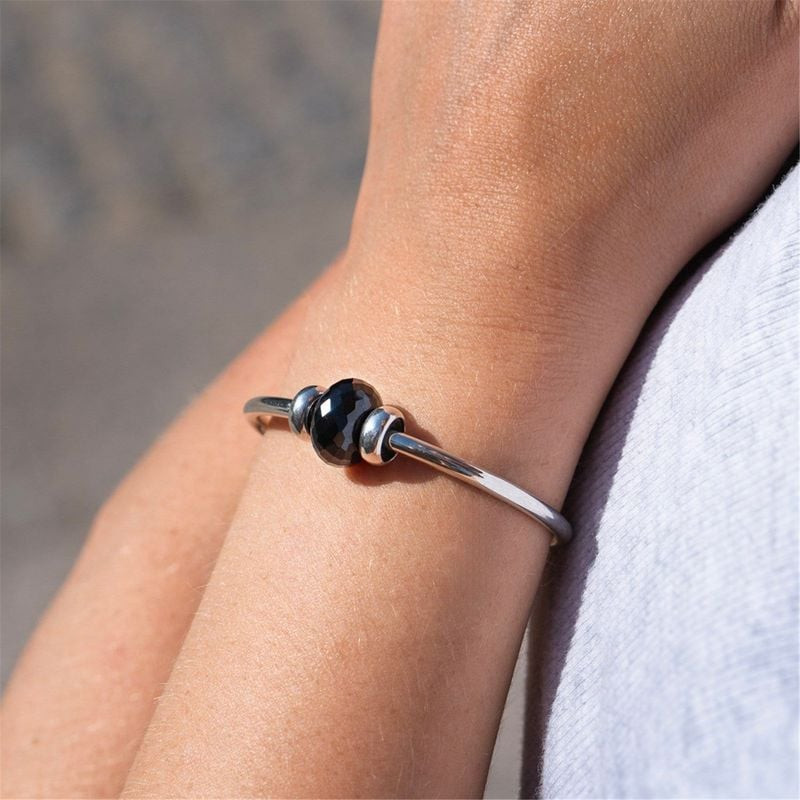 Femme portant une perle Trollbeads Onyx Noir sur un bracelet jonc argenté fin, en pleine lumière