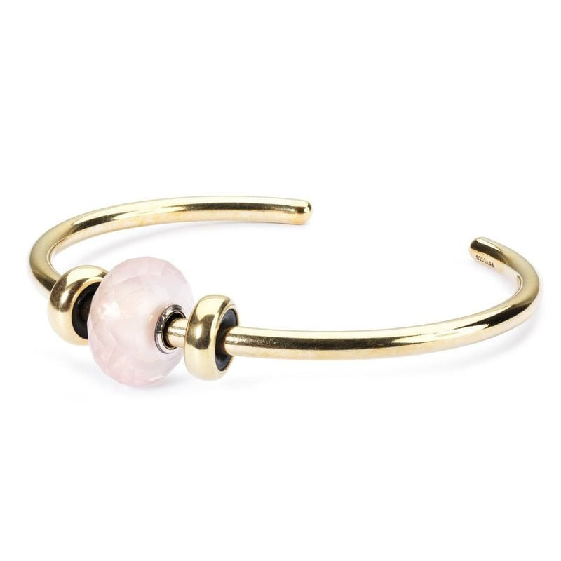 Bracelet manchette doré avec une perle Trollbeads en quartz rose et des intercalaires dorés.