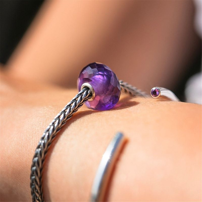 Breloque Trollbeads Améthyste portée sur un bracelet argenté au poignet d'une femme dans une lumière