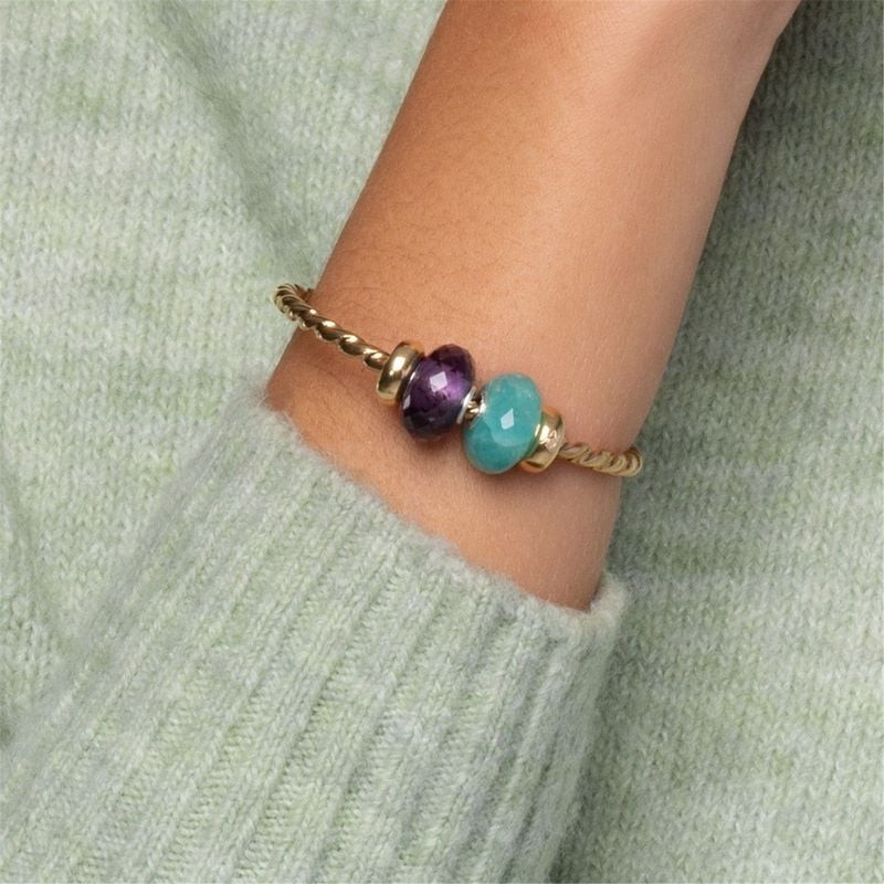 Perle Trollbeads améthyste sur un bracelet en or près d'une perle turquoise sur une manche en maille