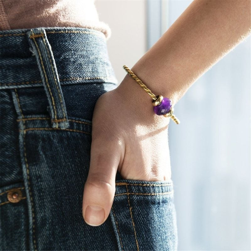 Breloque Trollbeads en améthyste violette sur bracelet doré, main posée dans une poche de jean